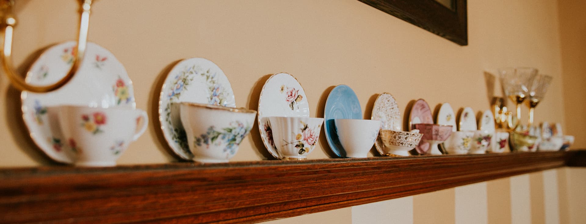 A variety of colorful china teacups and plates displayed on a wooden shelf.