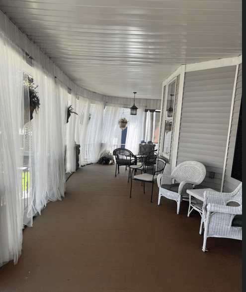 A cozy porch lined with sheer curtains and adorned with various chairs and hanging plants.