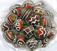 A close-up view of chocolate-covered strawberries adorned with white drizzles, arranged in a decorative dish.
