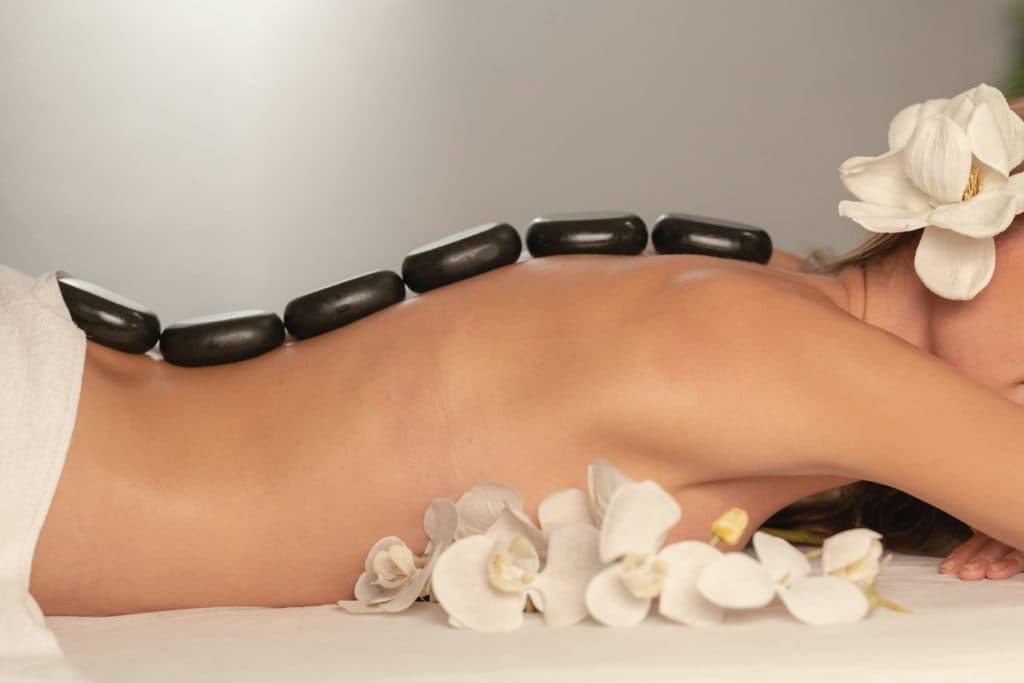 A person receiving a hot stone massage with white orchids placed nearby.