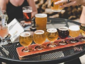 A flight of assorted craft beers on a table, with a hand pouring another drink.