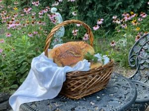 A woven basket with bread sits on a decorative table surrounded by flowers.