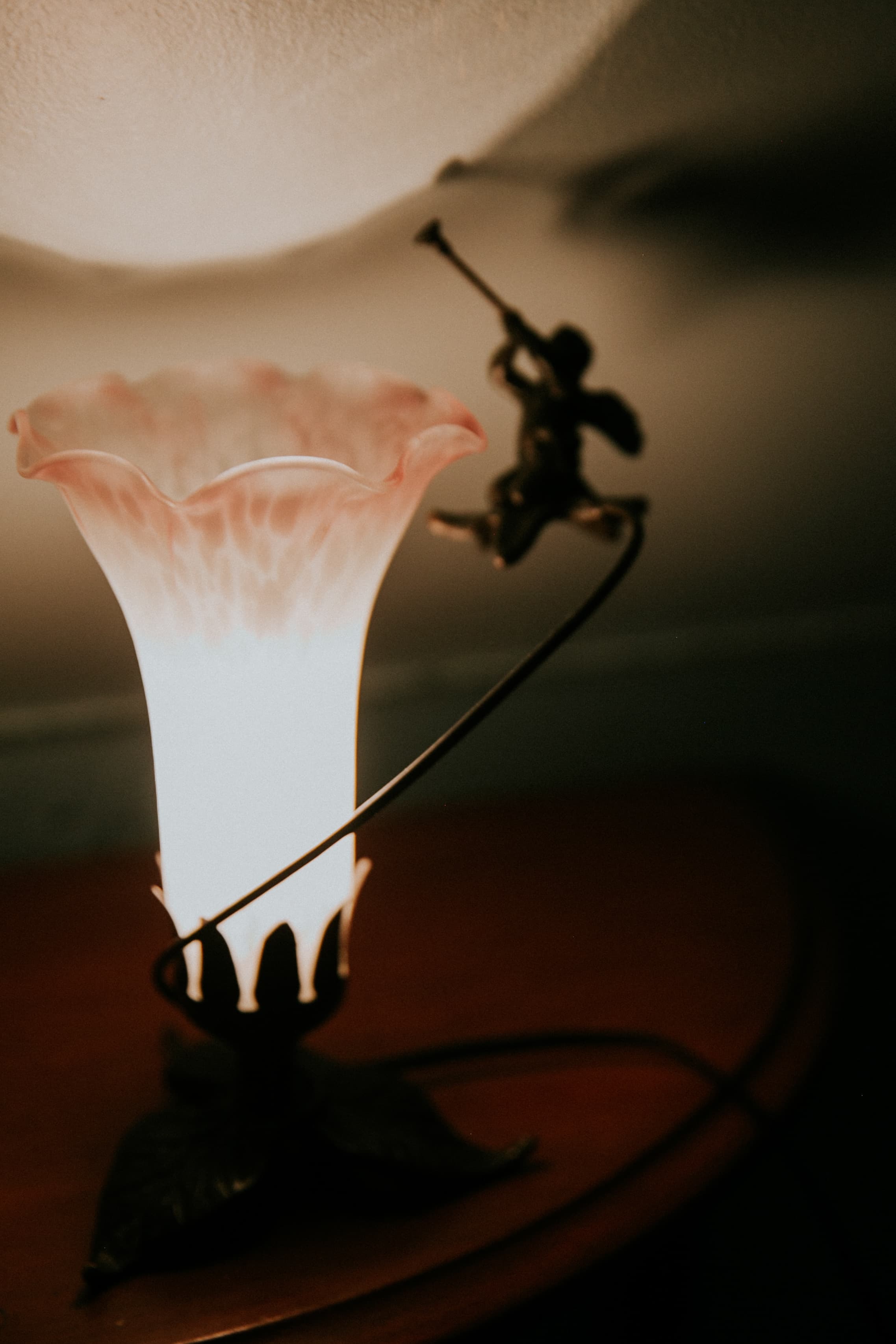 A decorative lamp with a pink glass shade and a trumpet-playing figure.