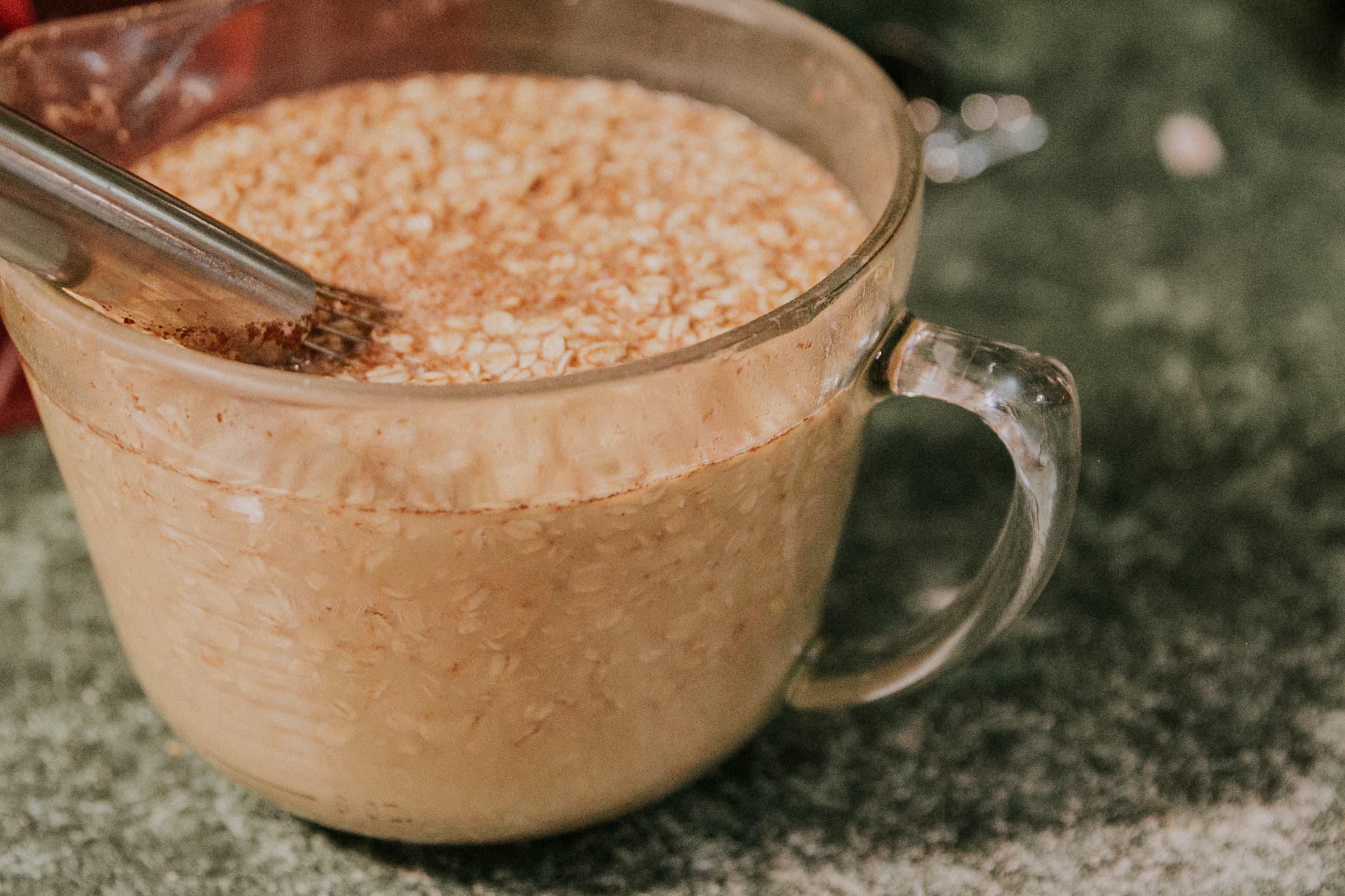 A clear measuring cup filled with oatmeal and a whisk resting inside.