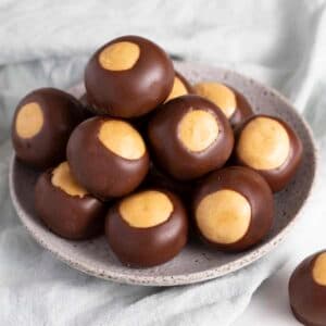 A plate stacked with round chocolate-covered treats featuring a creamy peanut butter center.
