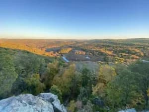 A panoramic view of rolling hills and valleys with autumn foliage under a clear blue sky.