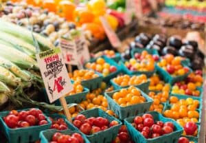 A vibrant market display featuring various baskets of fresh, colorful tomatoes and other produce.