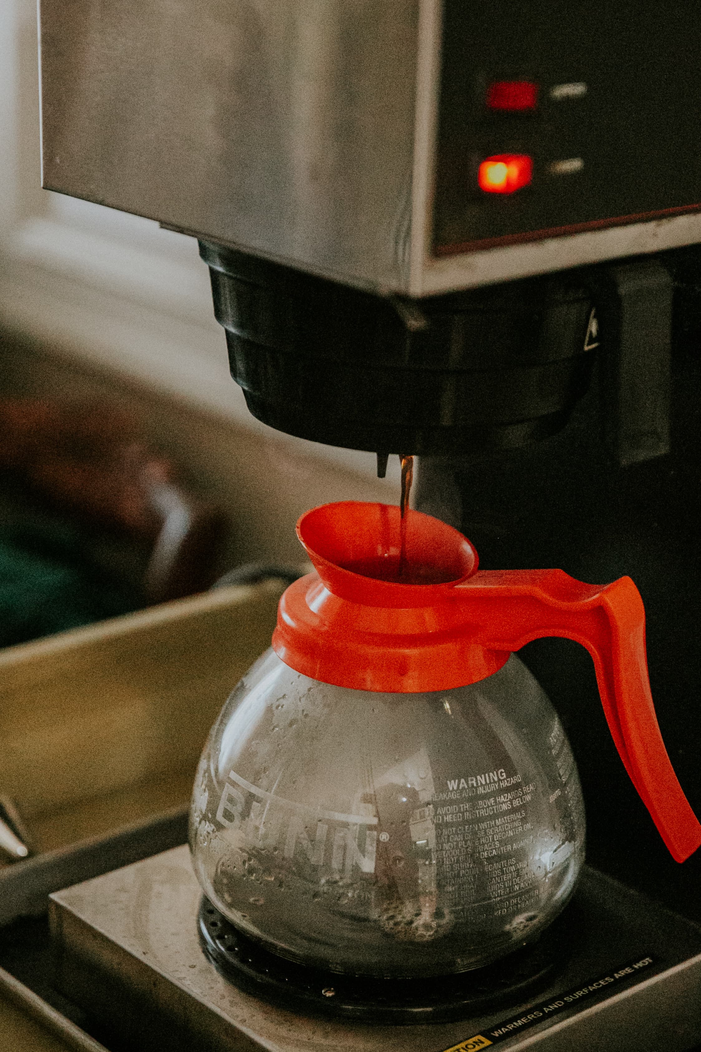 A coffee maker drips freshly brewed coffee into a glass carafe with a red handle.