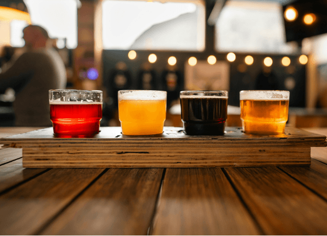 A flight of four colorful craft beers resting on a wooden tray in a cozy bar setting.