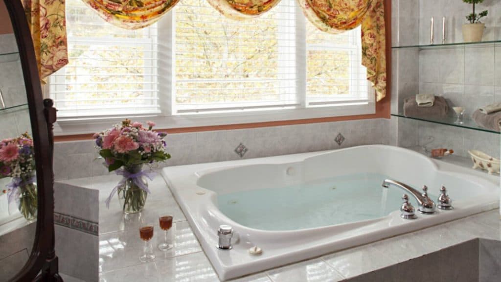 A luxurious bathroom featuring a spacious whirlpool tub, flowers, and decorative curtains.
