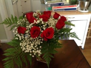 A bouquet of red roses surrounded by white baby's breath and greenery on a wooden table.