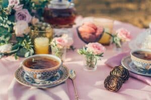A beautifully arranged tea set with floral decorations and desserts on a pink tablecloth.