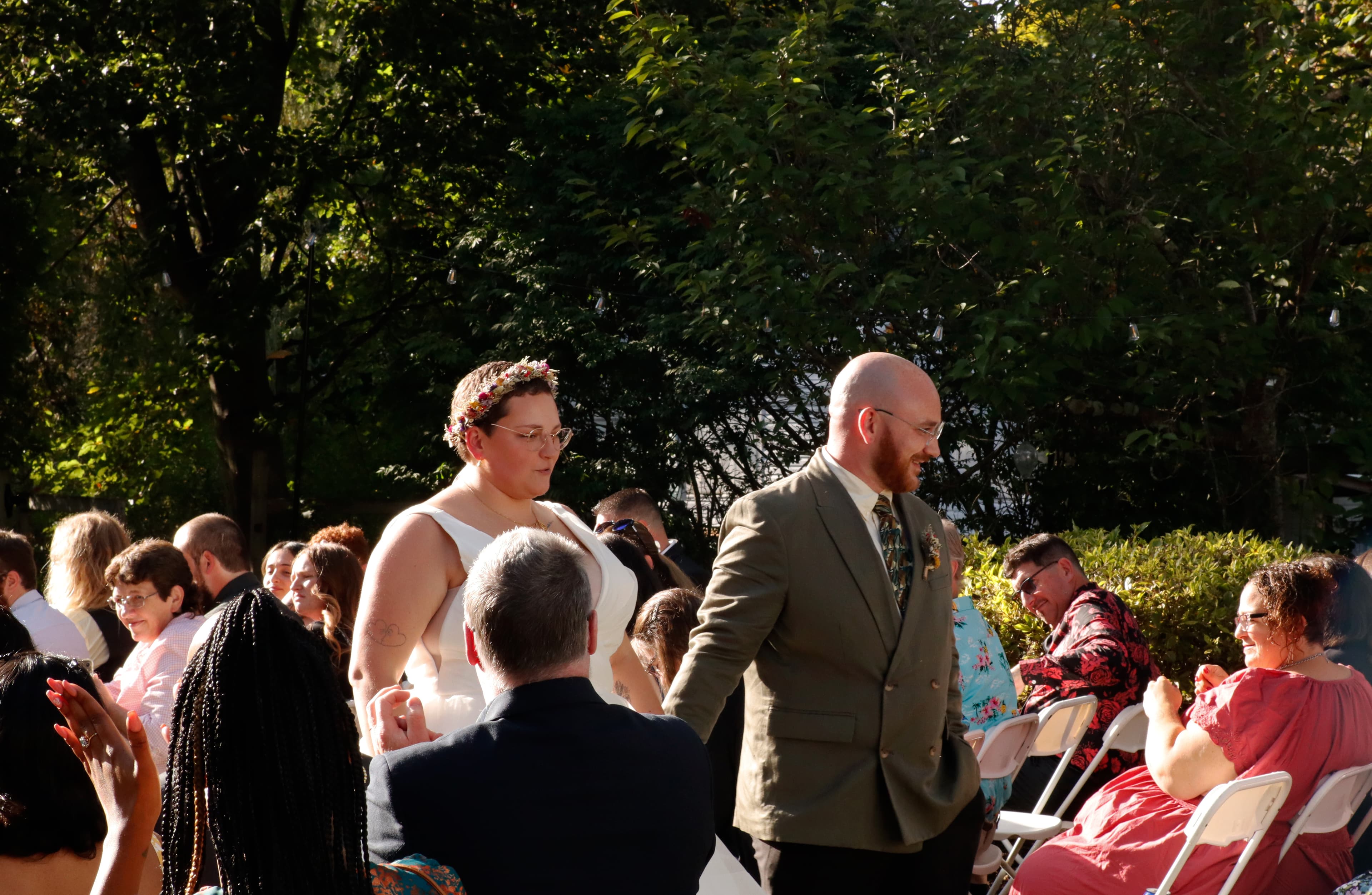 A couple walks down the aisle during a wedding ceremony, surrounded by seated guests.