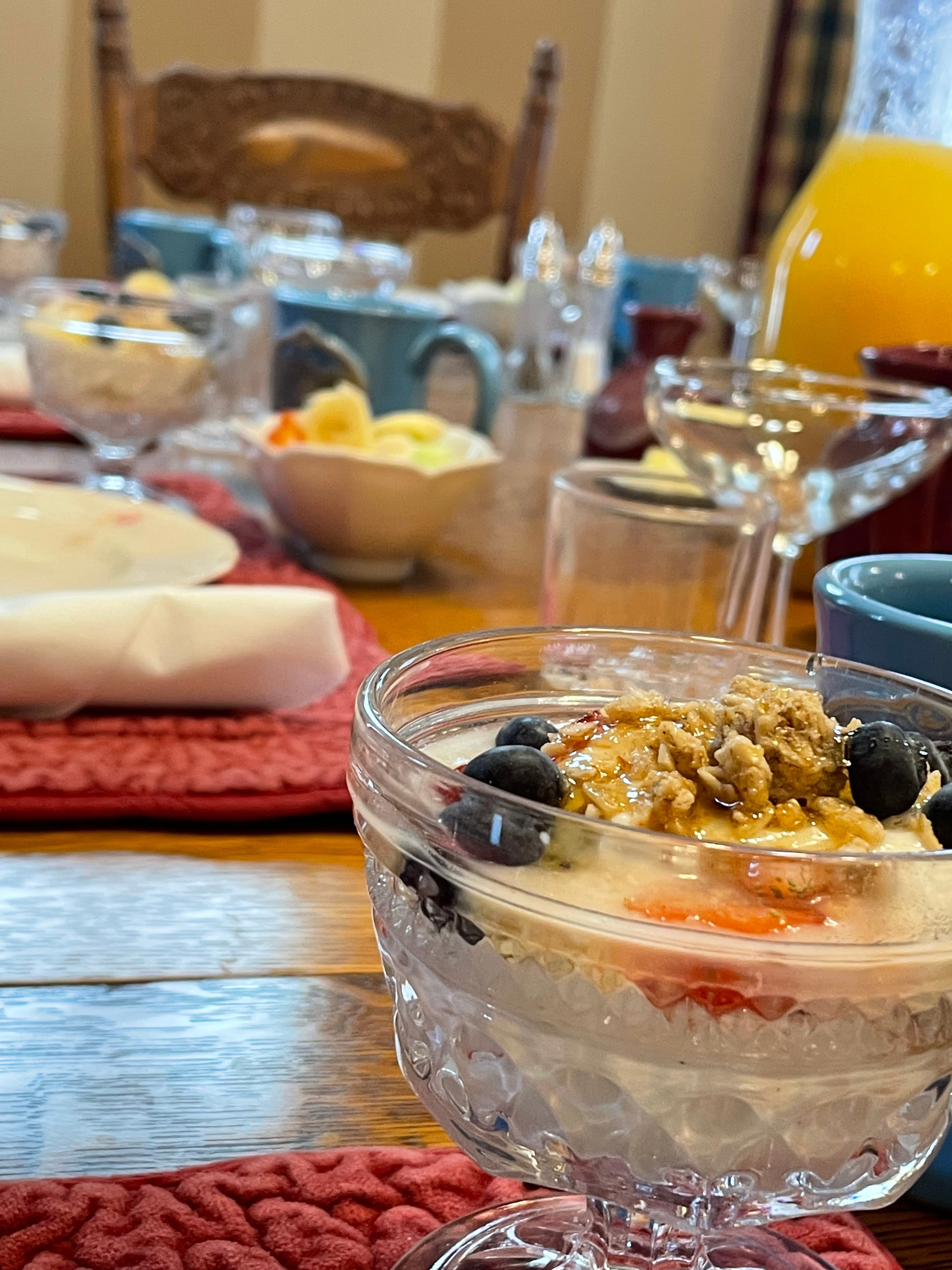 A beautifully set dining table featuring a glass dessert dish with yogurt, berries, and granola.