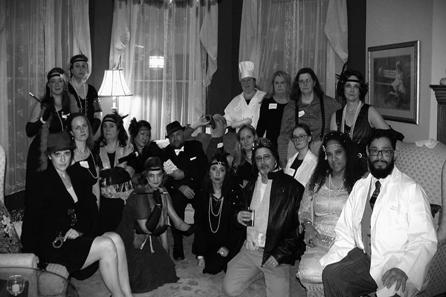 A group of people dressed in vintage attire poses together in a warmly lit room.