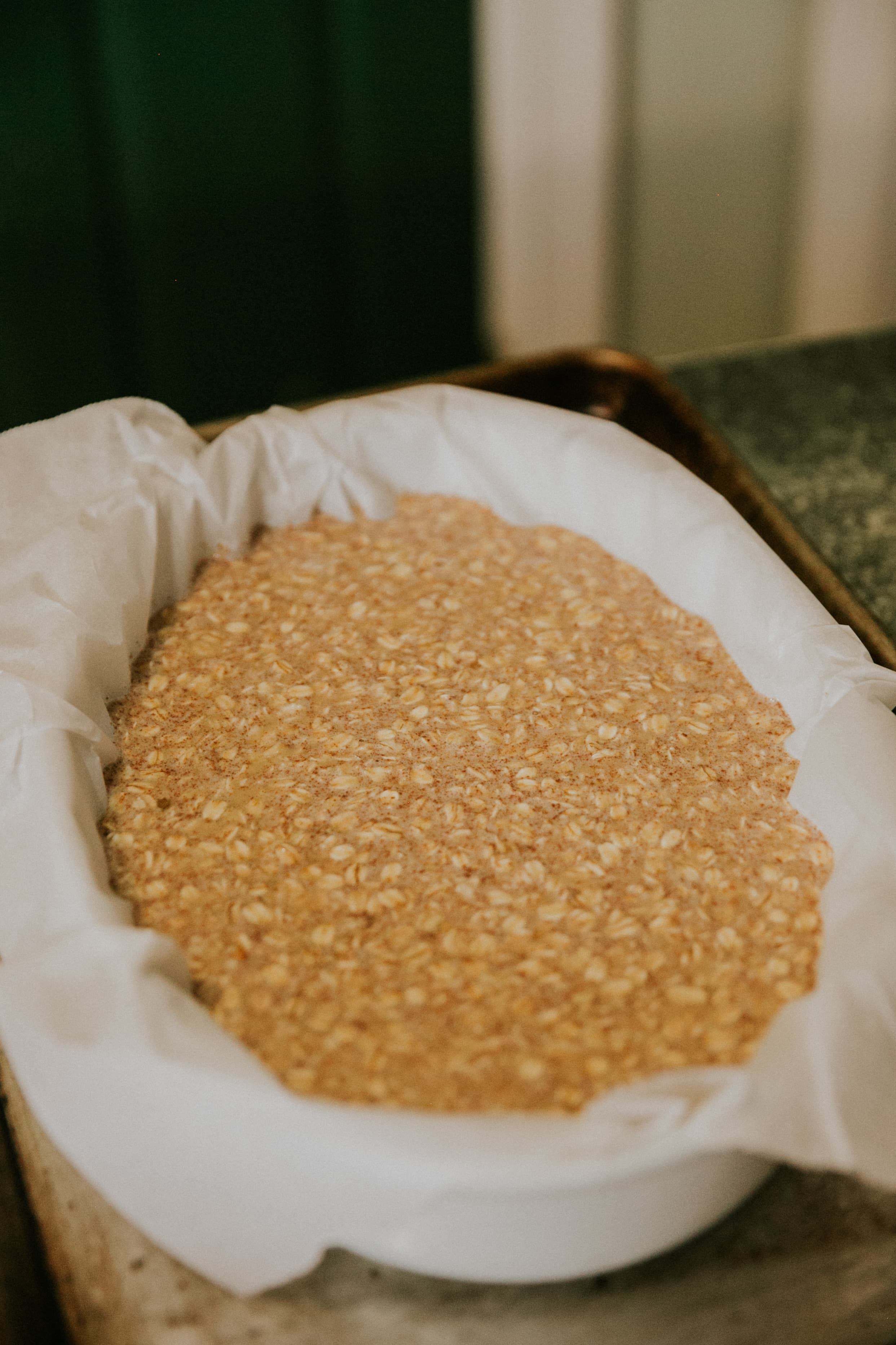 A baking dish lined with parchment paper filled with an uncooked mixture of oats. A baking dish lined with parchment paper filled with an uncooked mixture of oats.