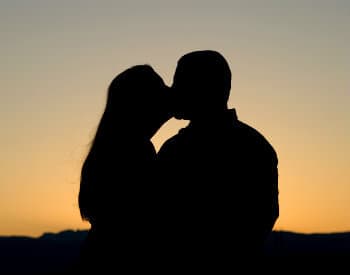Silhouetted couple kissing against a sunset.