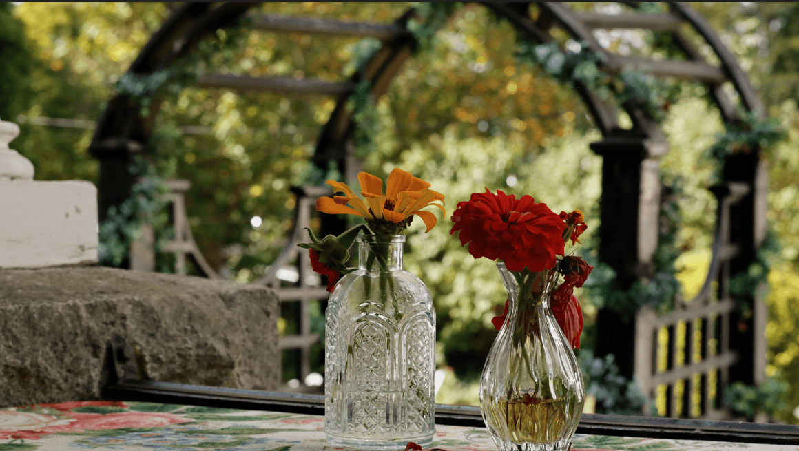 Two glass vases with colorful flowers sit on a table, framed by an ornate garden archway.