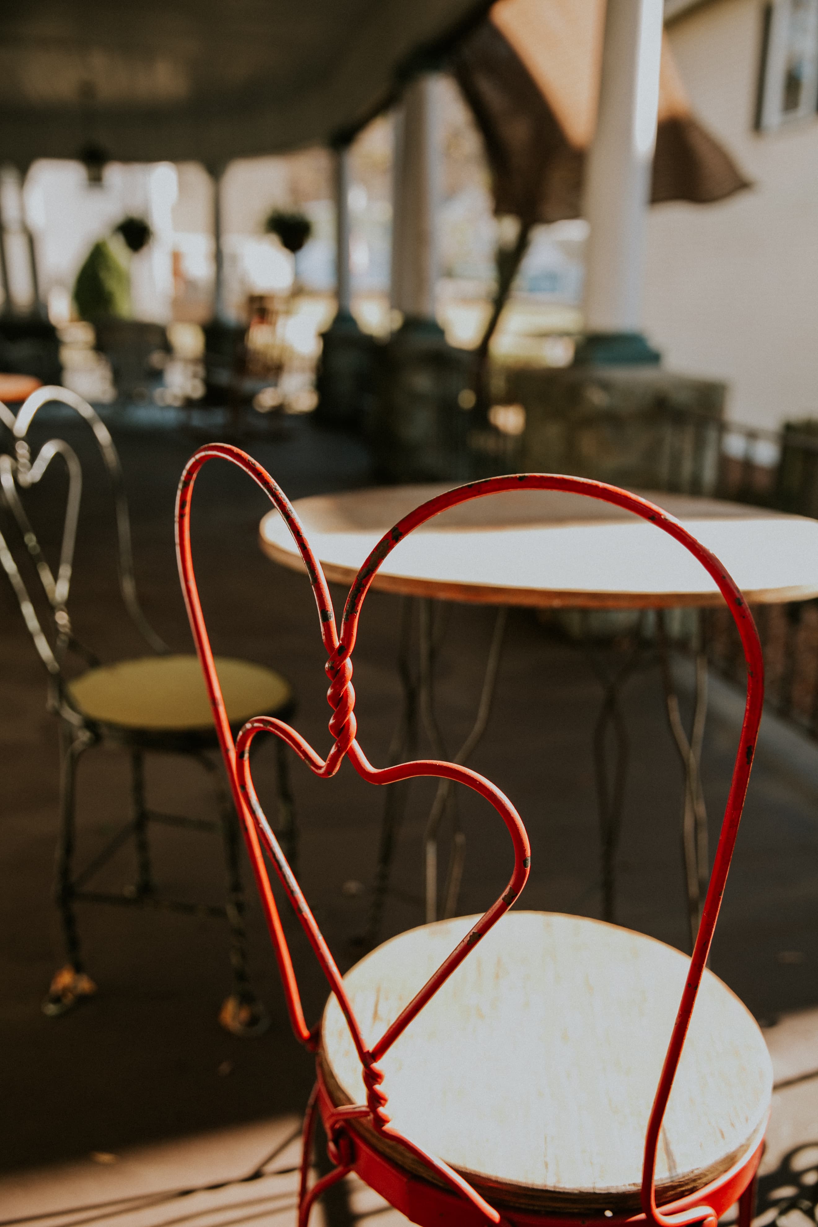 A red chair with a heart-shaped backrest is positioned next to a circular table on a patio.