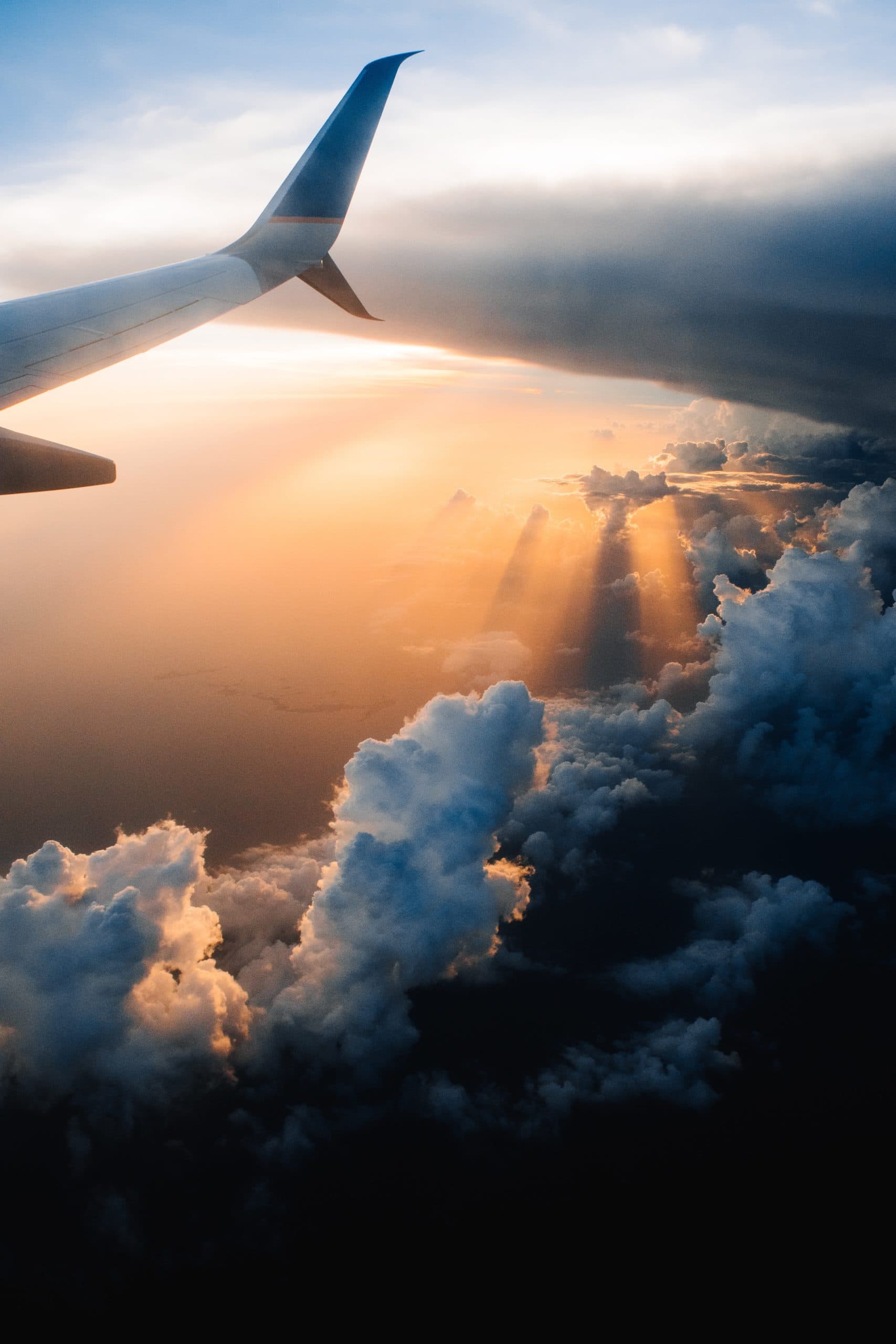Airplane wing above clouds with golden sunset rays.