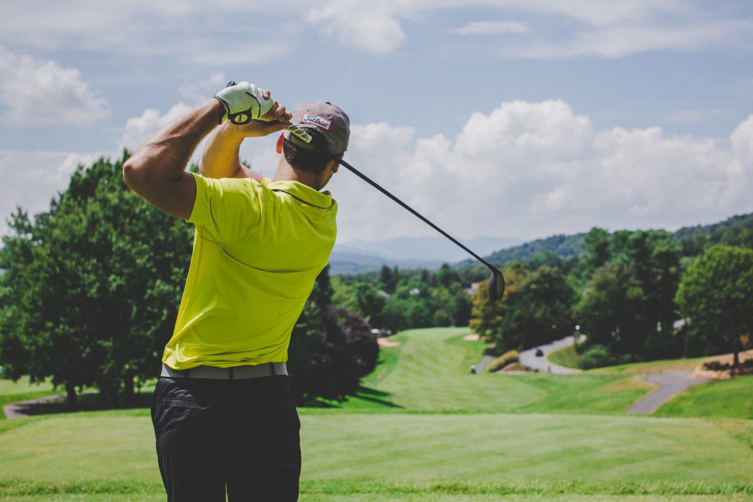 A golfer in a bright yellow shirt swings a club on a lush green course under a blue sky.