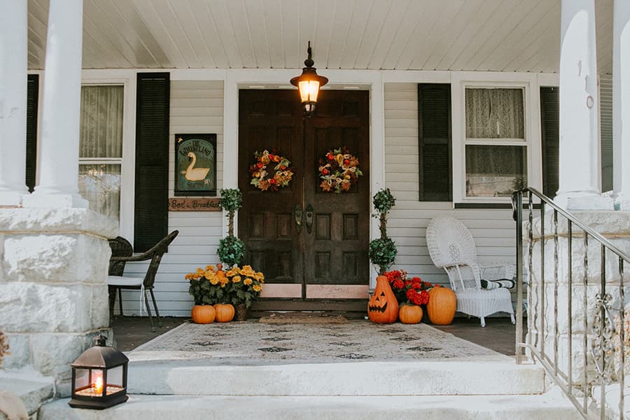 A cozy front porch decorated with fall flowers, pumpkins, and festive wreaths.