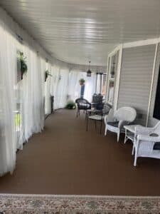 A cozy, screened-in porch with white curtains and wicker furniture.