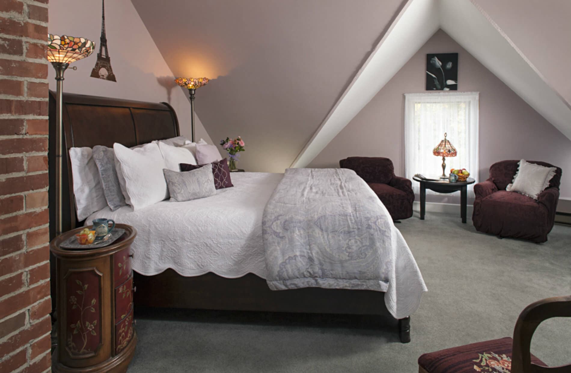 Cozy attic bedroom featuring a king-sized bed, two armchairs, and soft lighting.