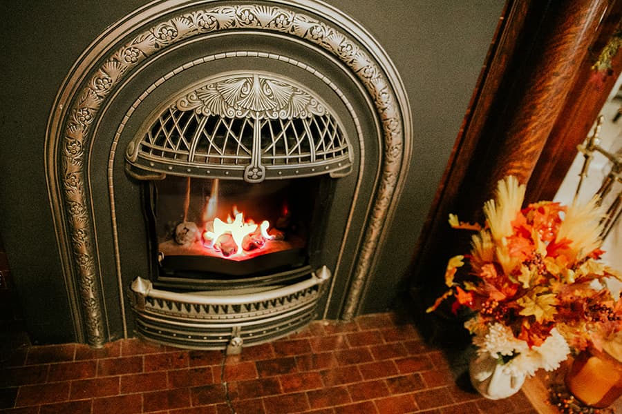A vintage fireplace with a glowing fire and a colorful autumn bouquet nearby.