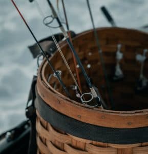 A wooden basket containing several fishing rods on a snowy surface.