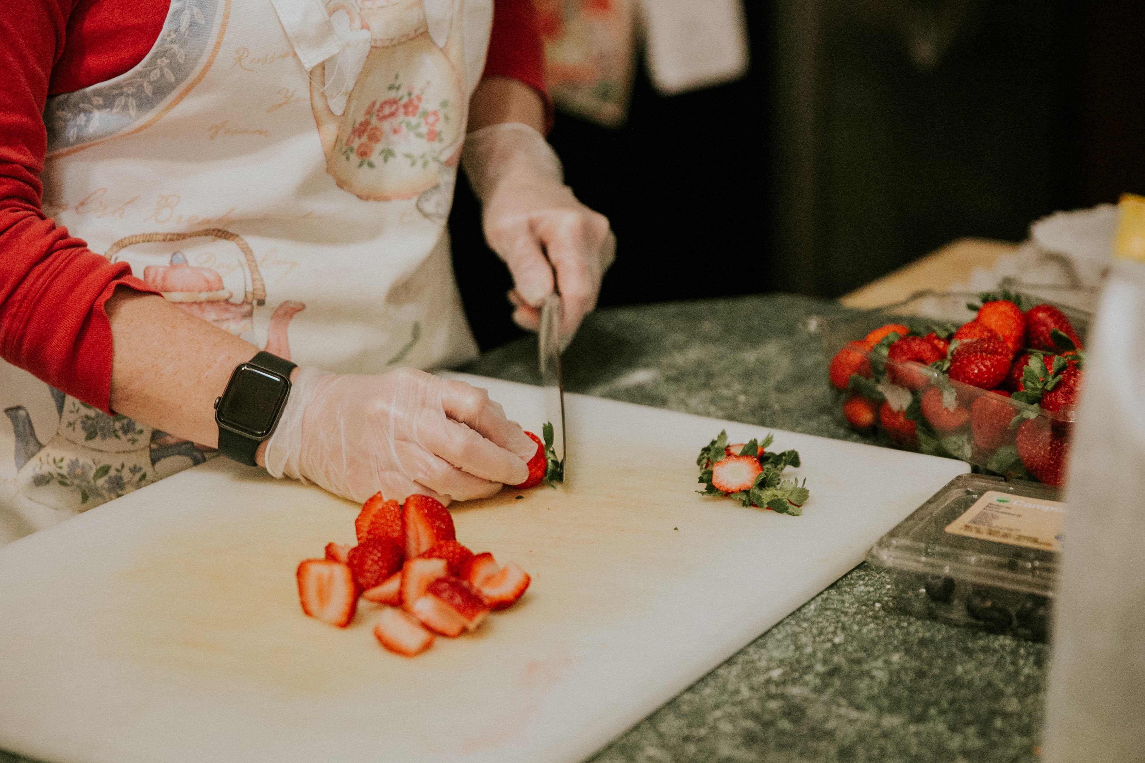 A person in a red shirt and apron is slicing strawberries on a cutting board.