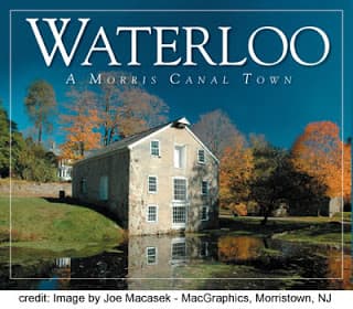 An old building reflected in a pond surrounded by colorful autumn trees, with the words "Waterloo: A Morris Canal Town" displayed above.