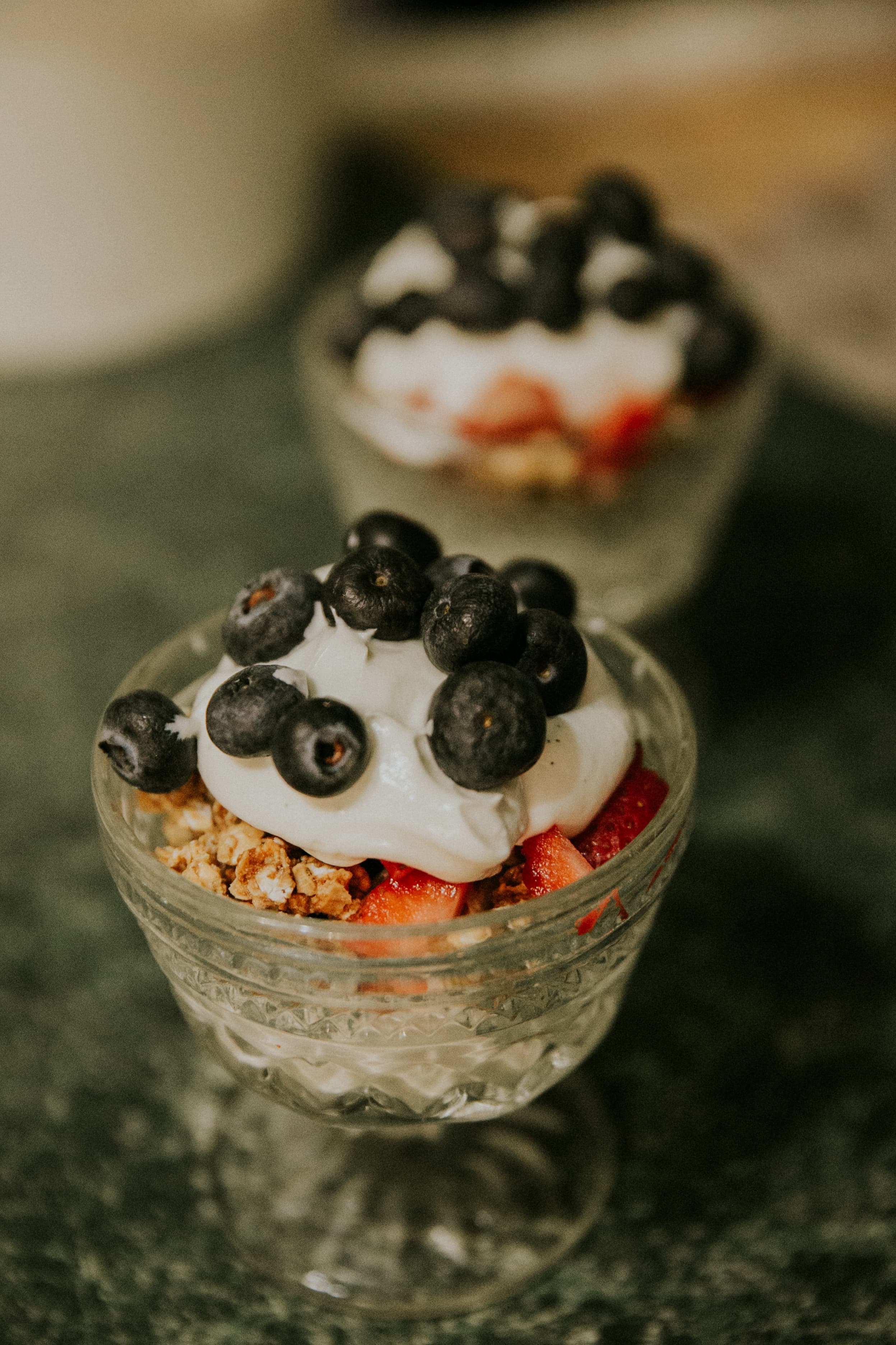 Two glass bowls filled with layers of granola, strawberries, whipped cream, and topped with blueberries.