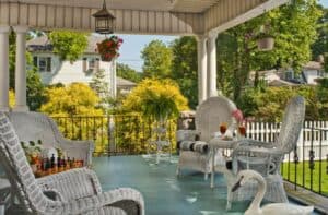 A cozy porch with white wicker furniture, a decorative swan, and lush greenery in the background.