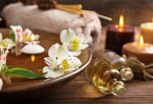 A wooden bowl filled with floating flowers, candles, and essential oils, creating a serene spa atmosphere.