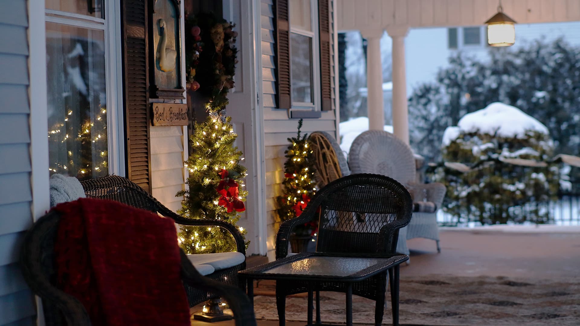 A cozy porch decorated with holiday lights and a red blanket, surrounded by snow.