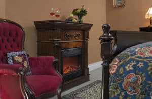 Wooden fireplace next to red wingback chair in tan walled bedroom