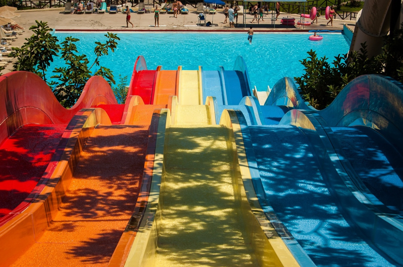 Five hilly waterslides in red, orange, yellow, and blue with a sparkling blue swimming pool at the bottom