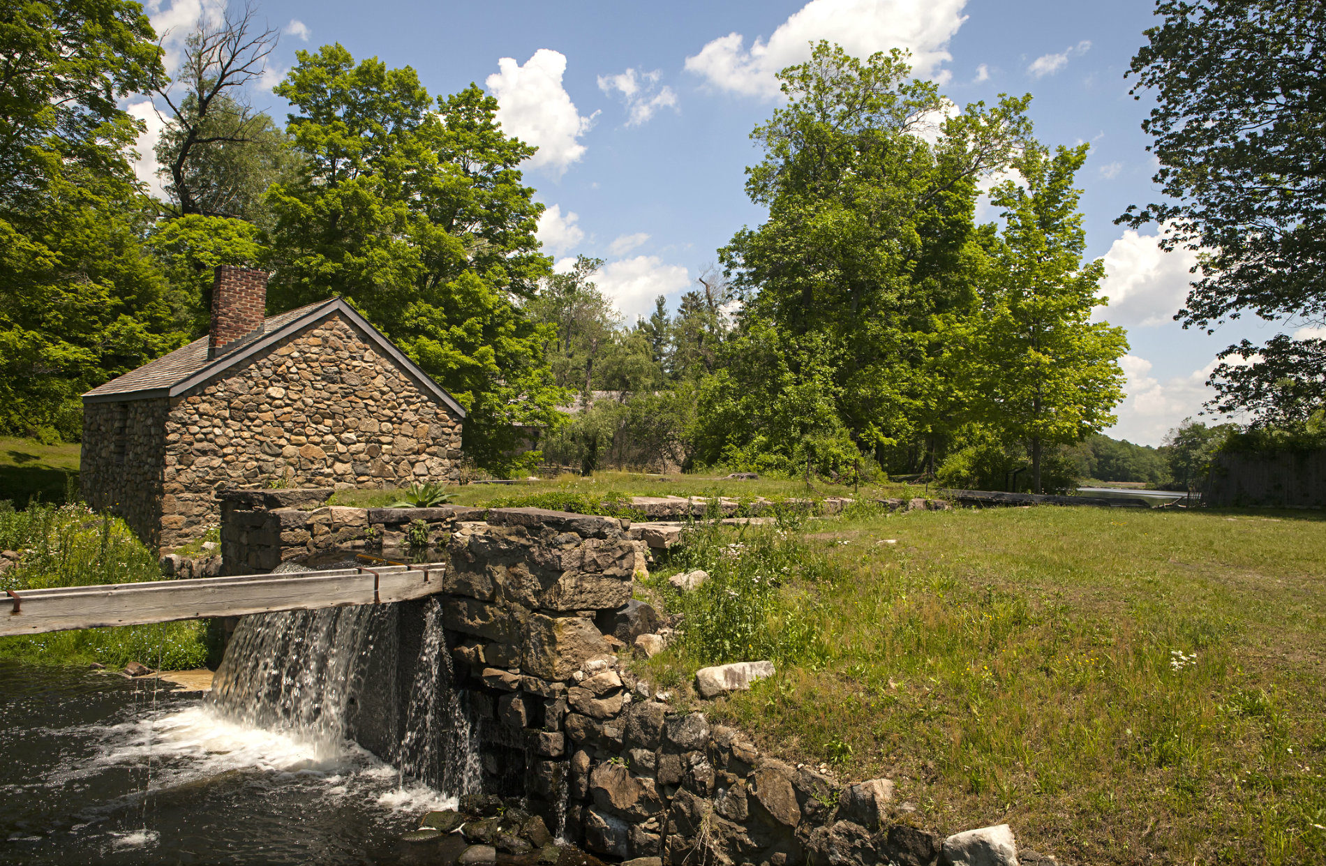 Stone mill house on river with green grass and trees