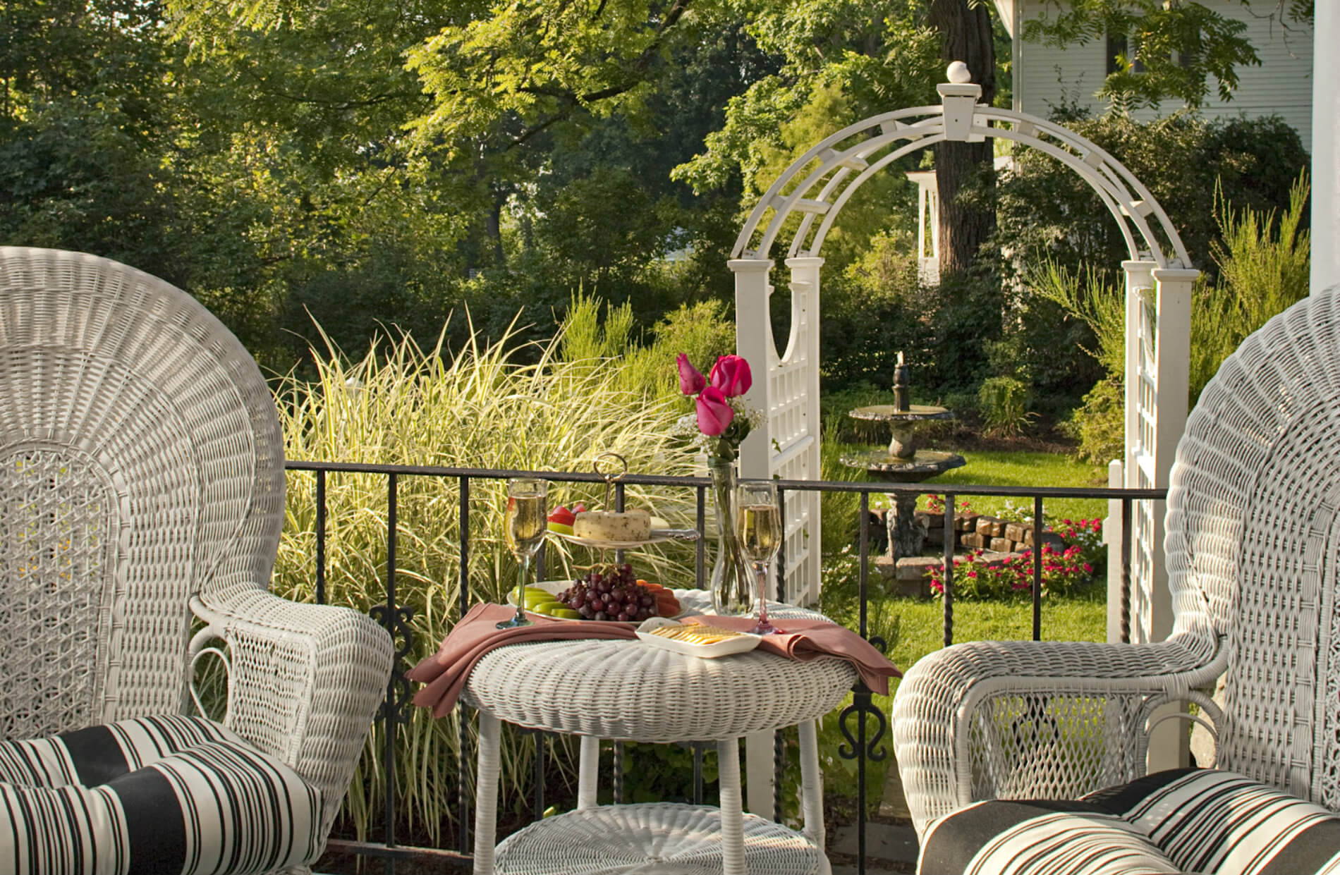 White wicher lawn furniture on porch with view of white arch in garden