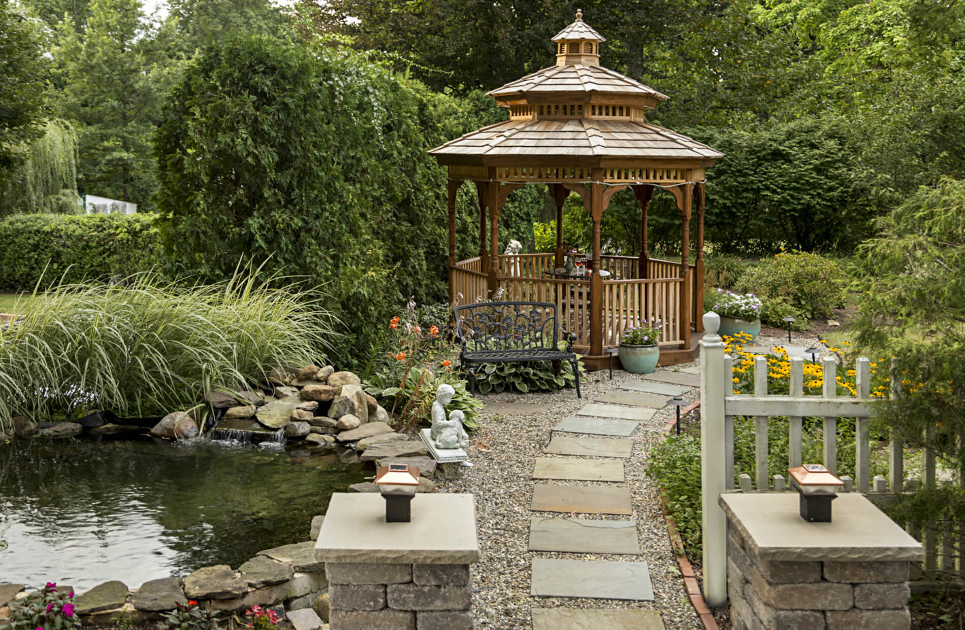 Stone path leading to wooden gazebo with green hedge in background