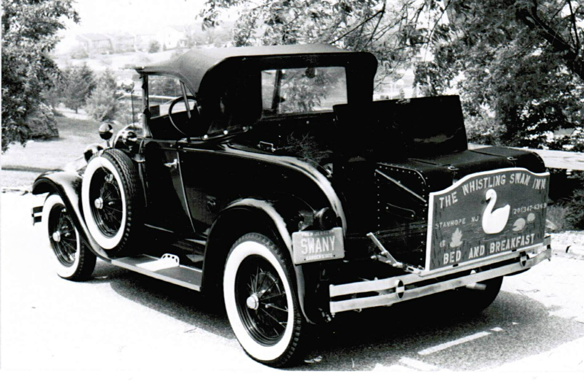 Antique black automobile with Whistling Swan Inn sign on back