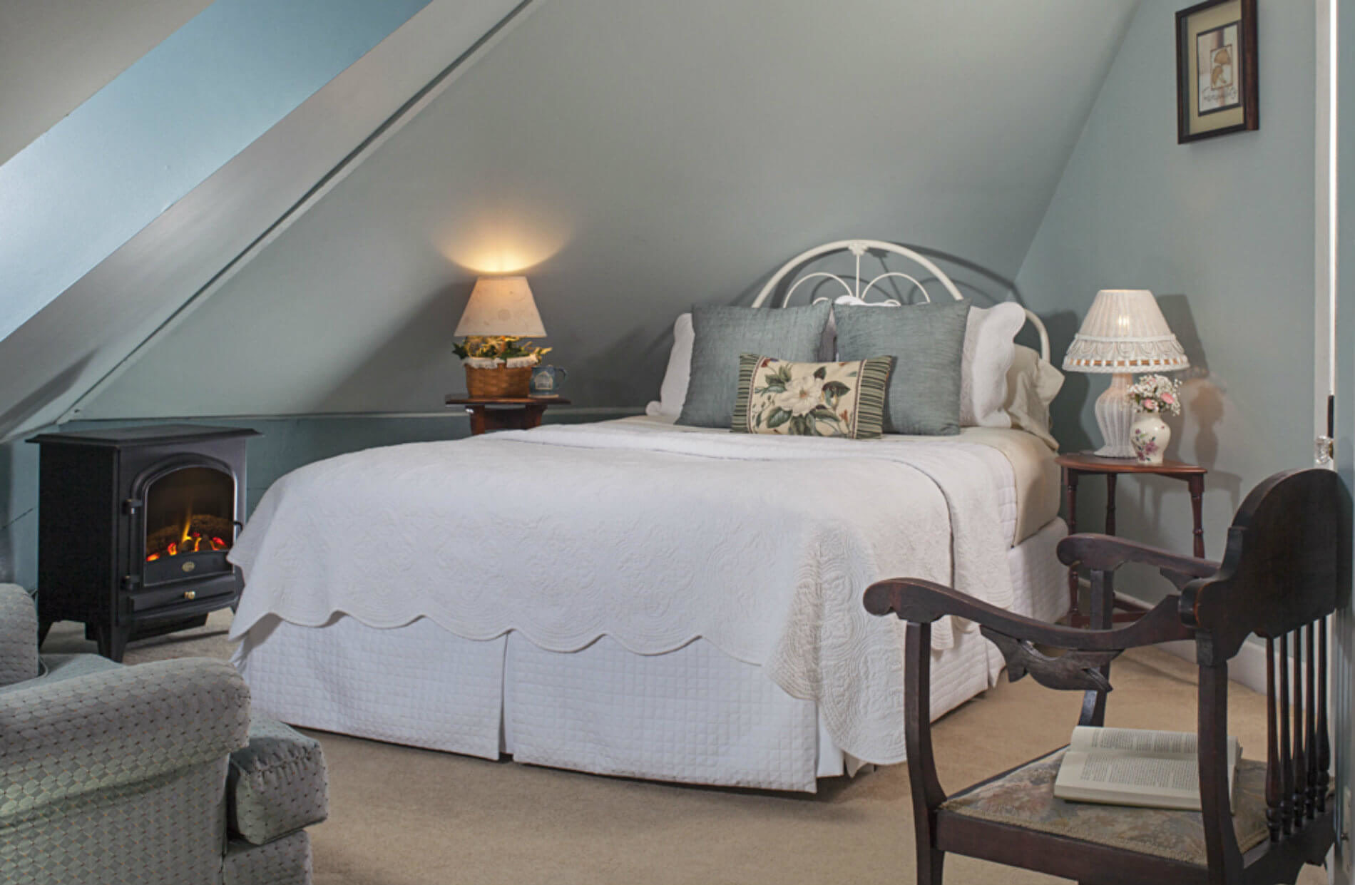 Large bed with white coverlet in gabled ceiling room with lamp