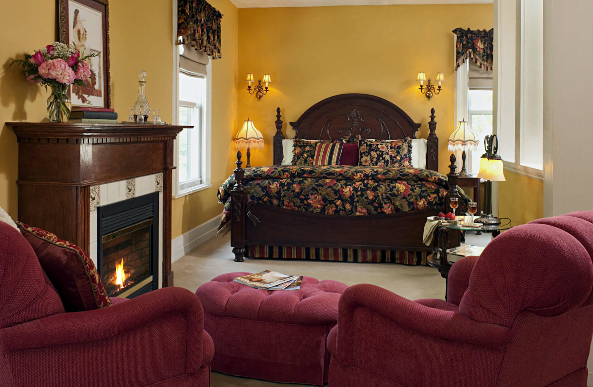 Gold walled room with large wooden bed with drk bedding and two red wingback chairs