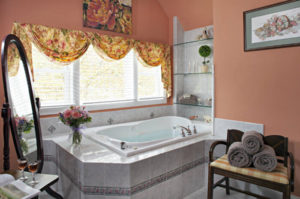 Large white tub surrounded by peach walls and a large window