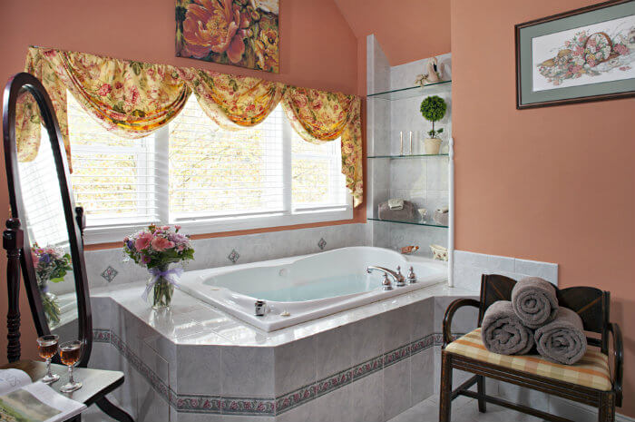 Large white tub surrounded by peach walls and a large window