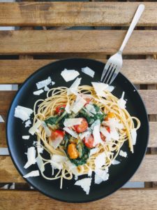 A pasta dish on a black ceramic plate, sitting atop a wooden table.