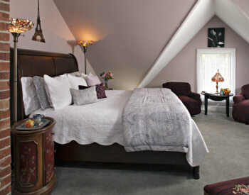 Dormered ceiling room with wooden bed with soft white bedding