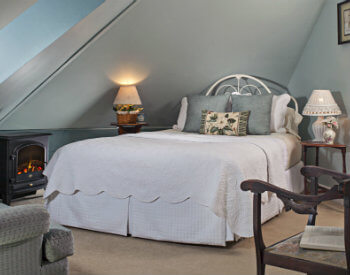 White iron bed with white coverlet in blue walled room with small fireplace