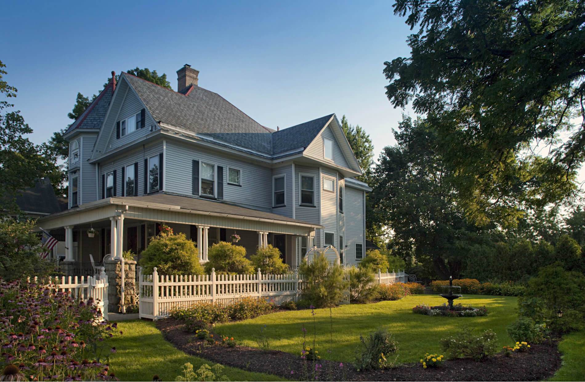 Large house with gabled roof surrounded by gree lwn and trees